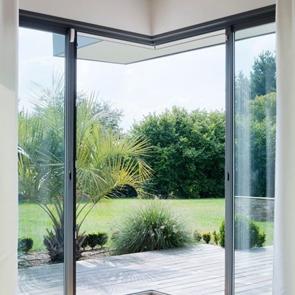 Baie vitrée en aluminium ouverte sur un jardin arboré, apportant luminosité et performance énergétique à l’habitat moderne.