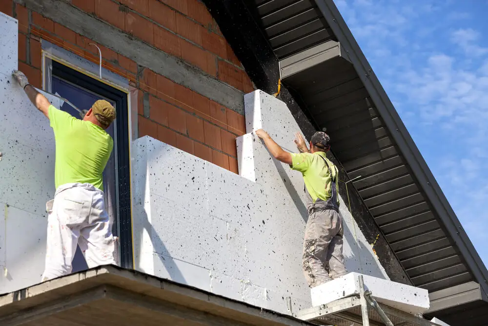 Deux ouvriers posent des panneaux isolants en polystyrène sur la façade d